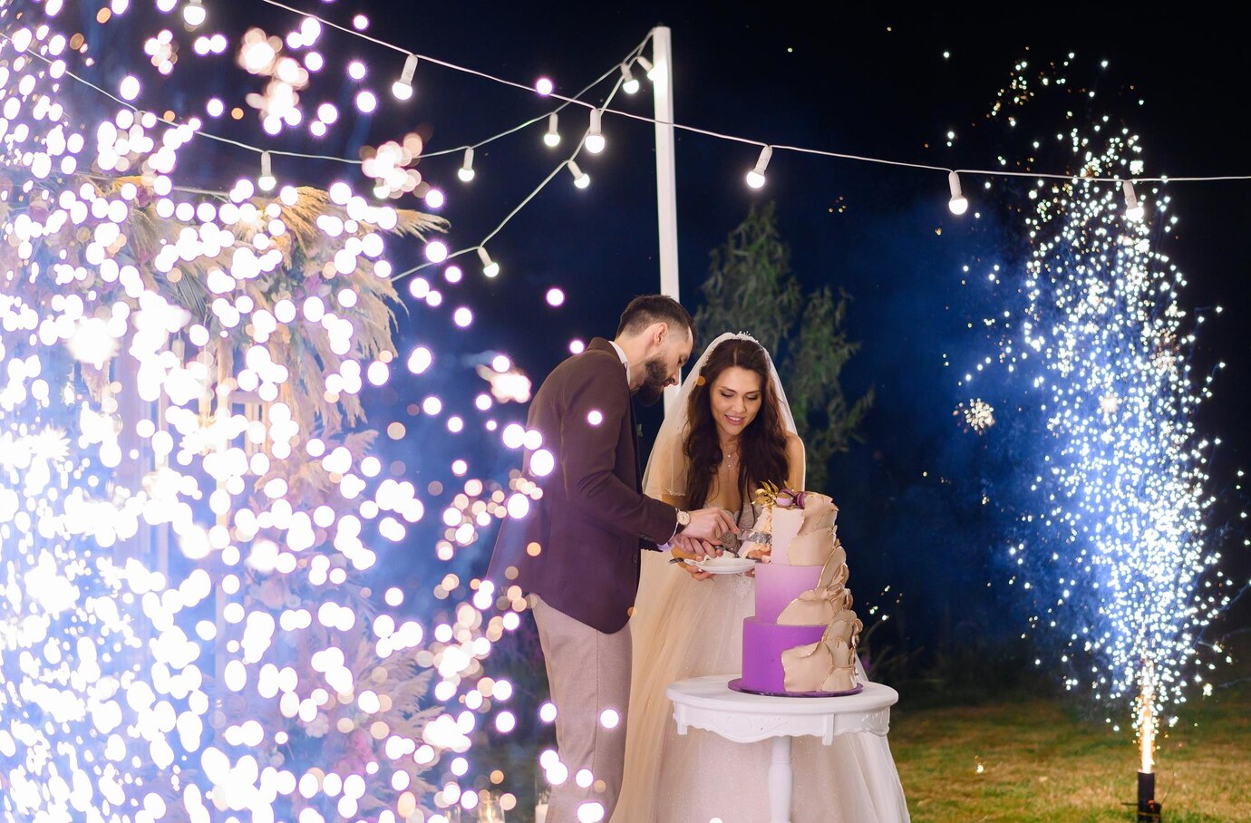 newlyweds-evening-celebration-wedding-cutting-cake-outdoors_8353-12541